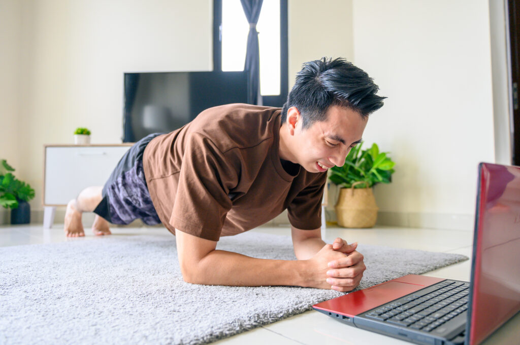 Asian man uses digital device for online fitness lessons plank pose